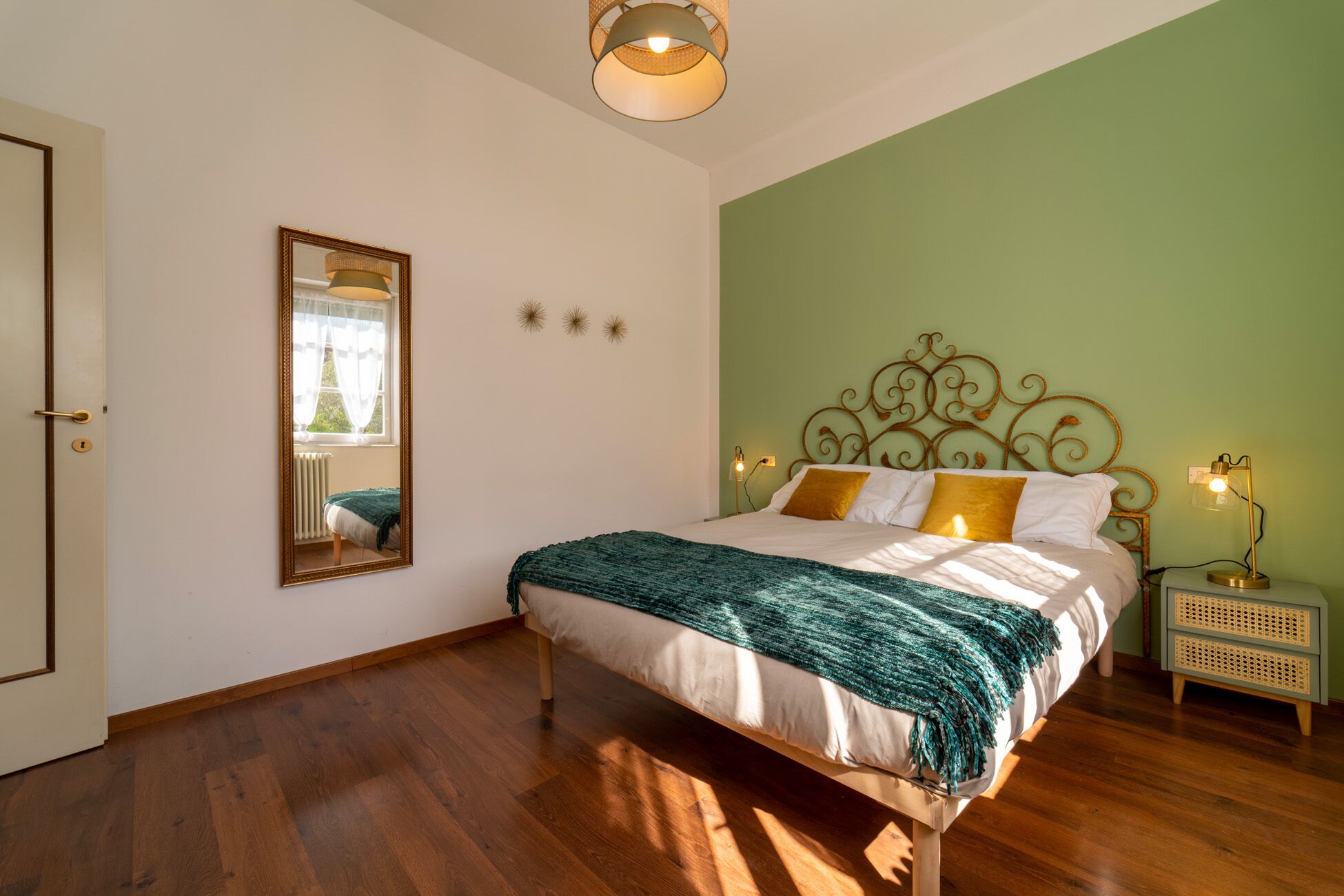 Un dormitorio con cama, mesita de noche, lámpara, espejo y puerta.