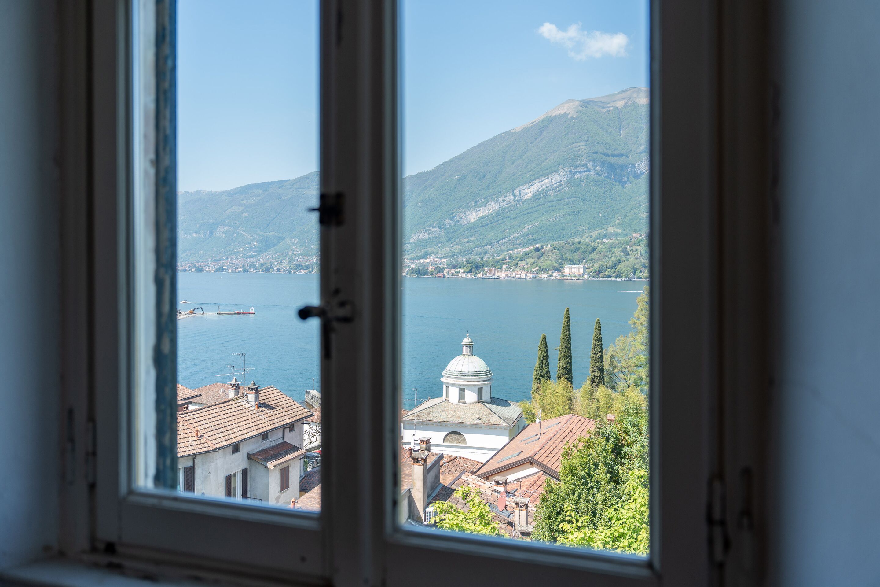 A window view of a lake with buildings and a mountain in the background.