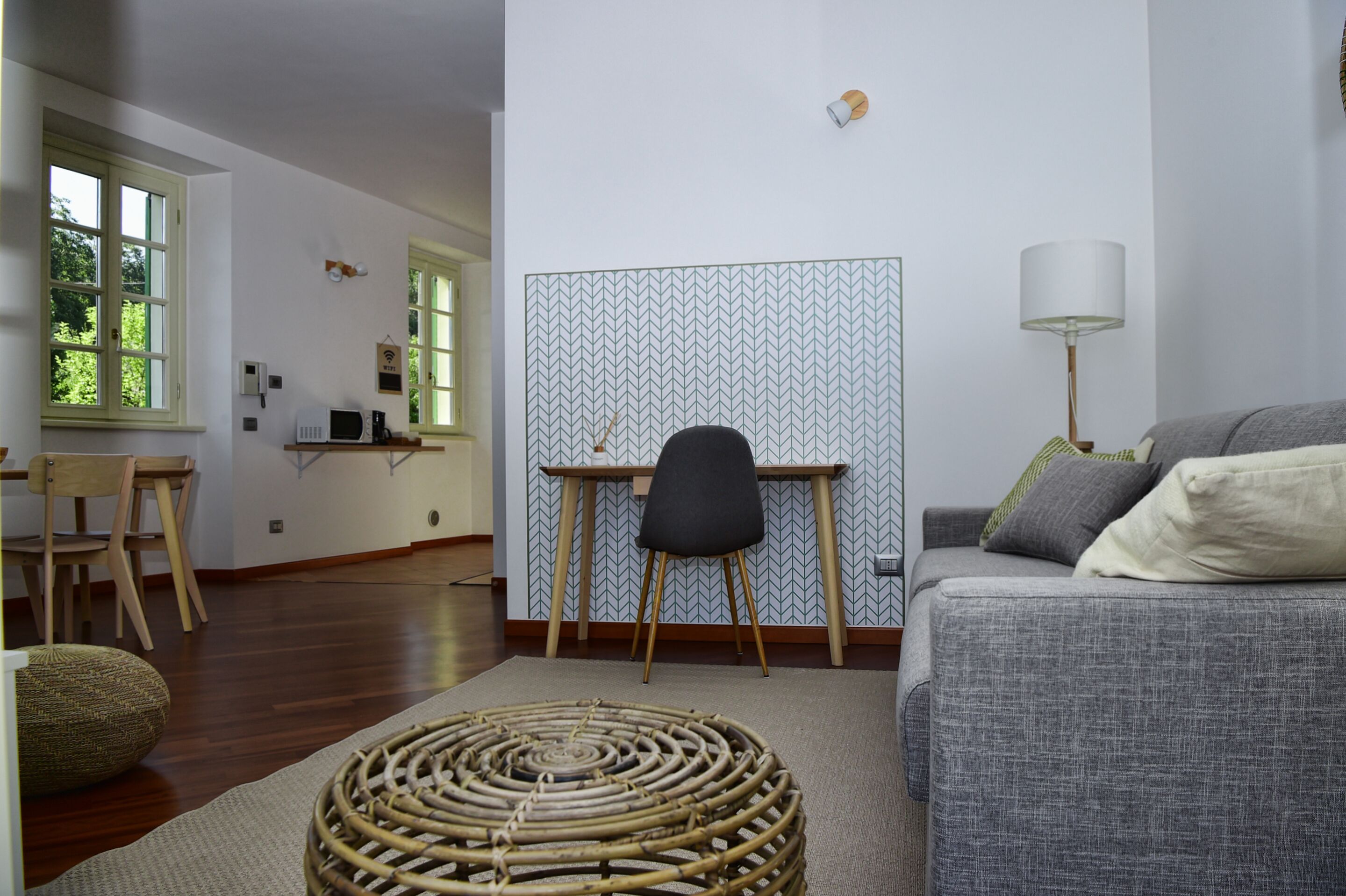 A modern living room with a grey sofa, a black chair, a woven floor mat, and a patterned wall.