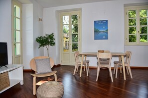 Un comedor con una mesa y sillas de madera, una planta en maceta y un televisor sobre un mueble blanco.