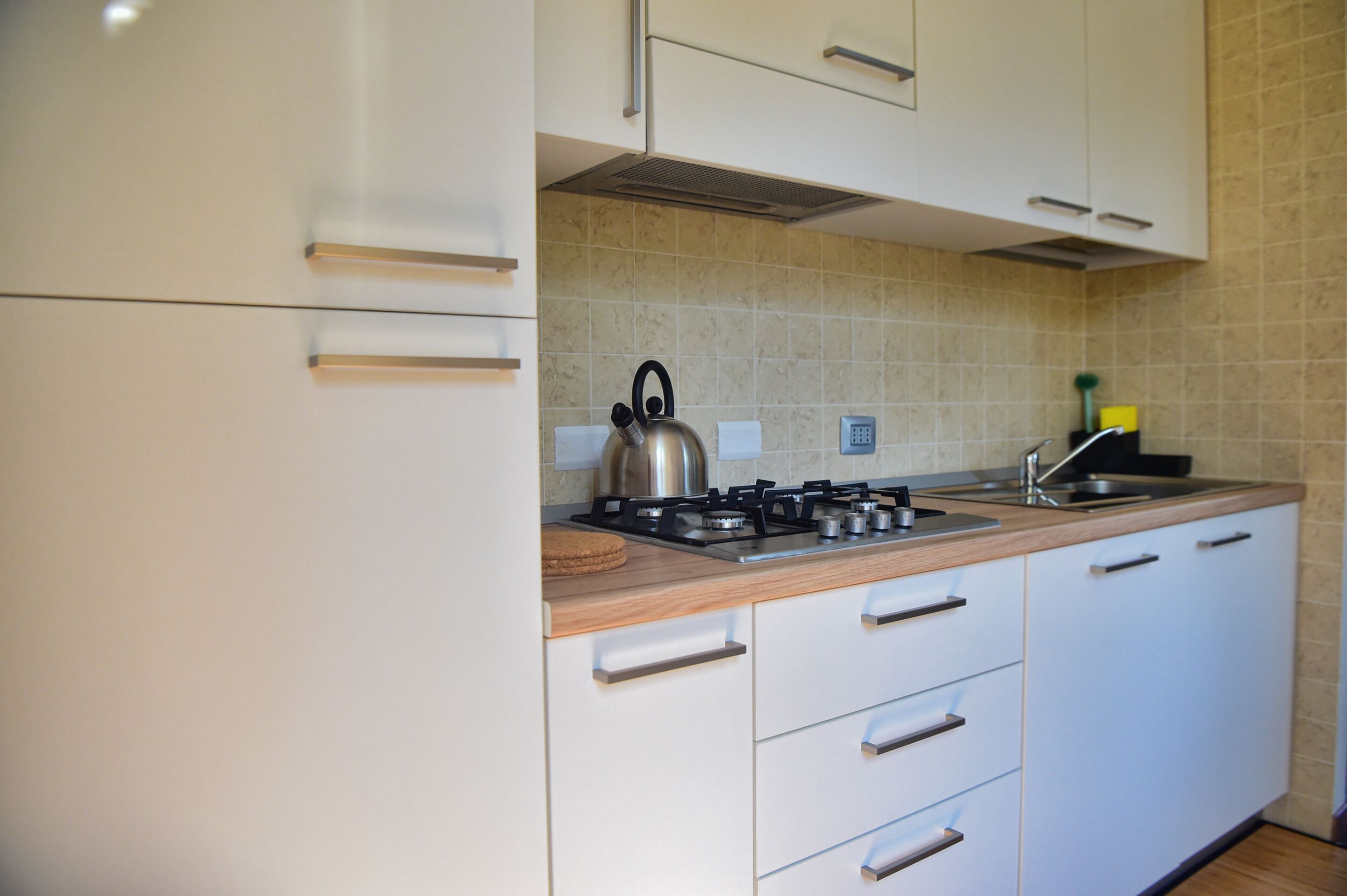 Una cocina moderna con armarios blancos, un hervidor de acero inoxidable y una estufa a gas.