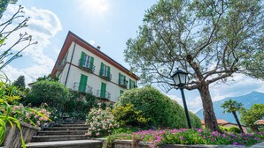 Un bâtiment doté d’un escalier menant à un balcon, entouré d’une végétation luxuriante et de fleurs.