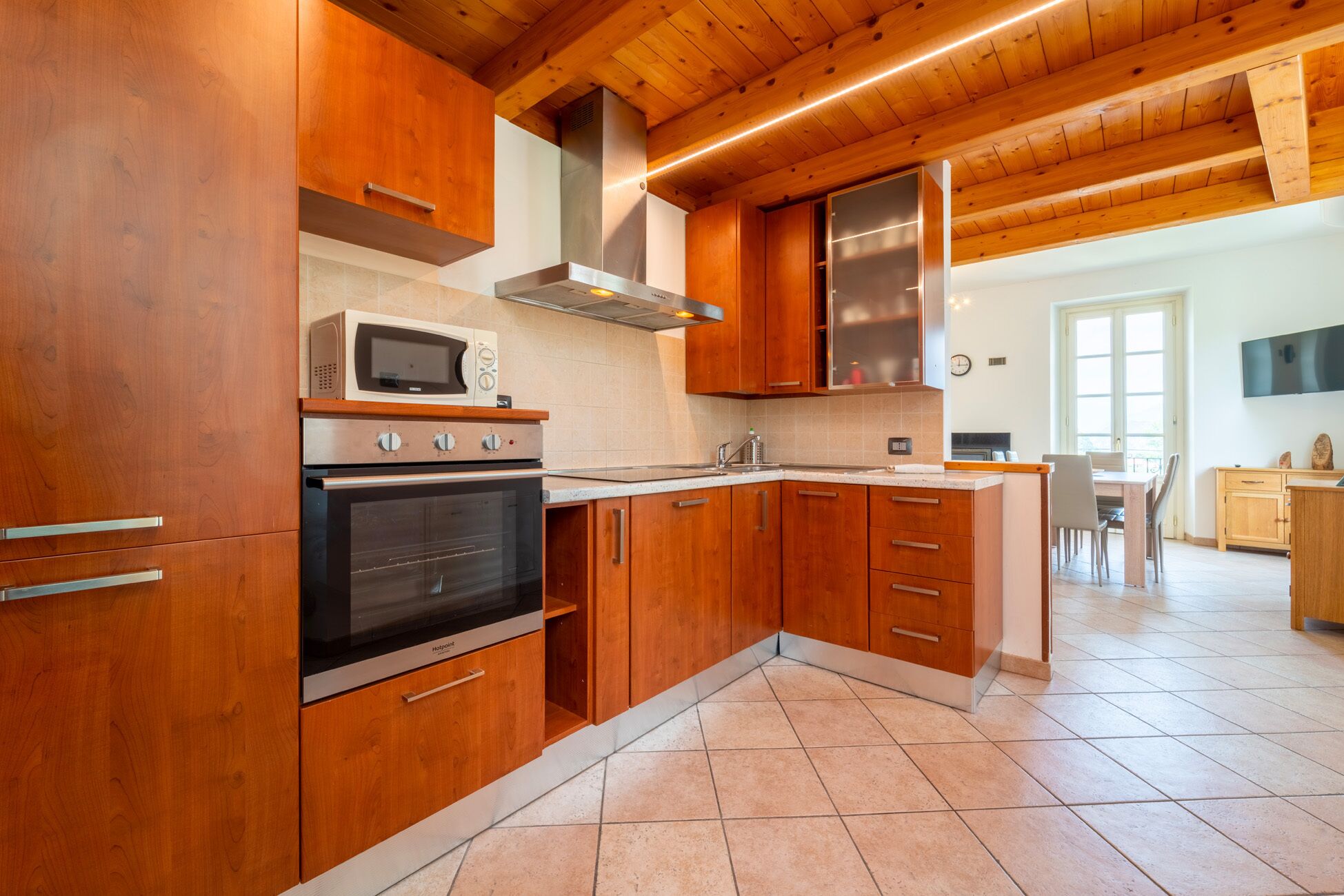 A modern kitchen with wooden cabinets, a built-in oven, a microwave, and a stainless steel range hood.