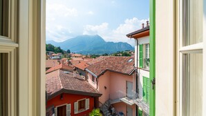 Une vue depuis une fenêtre donnant sur une ville aux toits de tuiles rouges, avec une montagne en arrière-plan et un bâtiment vert sur la droite.