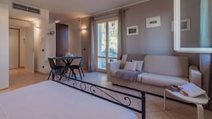 A modern hotel room with a bed, a sofa, a small table, and a balcony with a view. - Incanto Apartment - One Bedroom Apartment, Sleeps 2 (Bellagio)