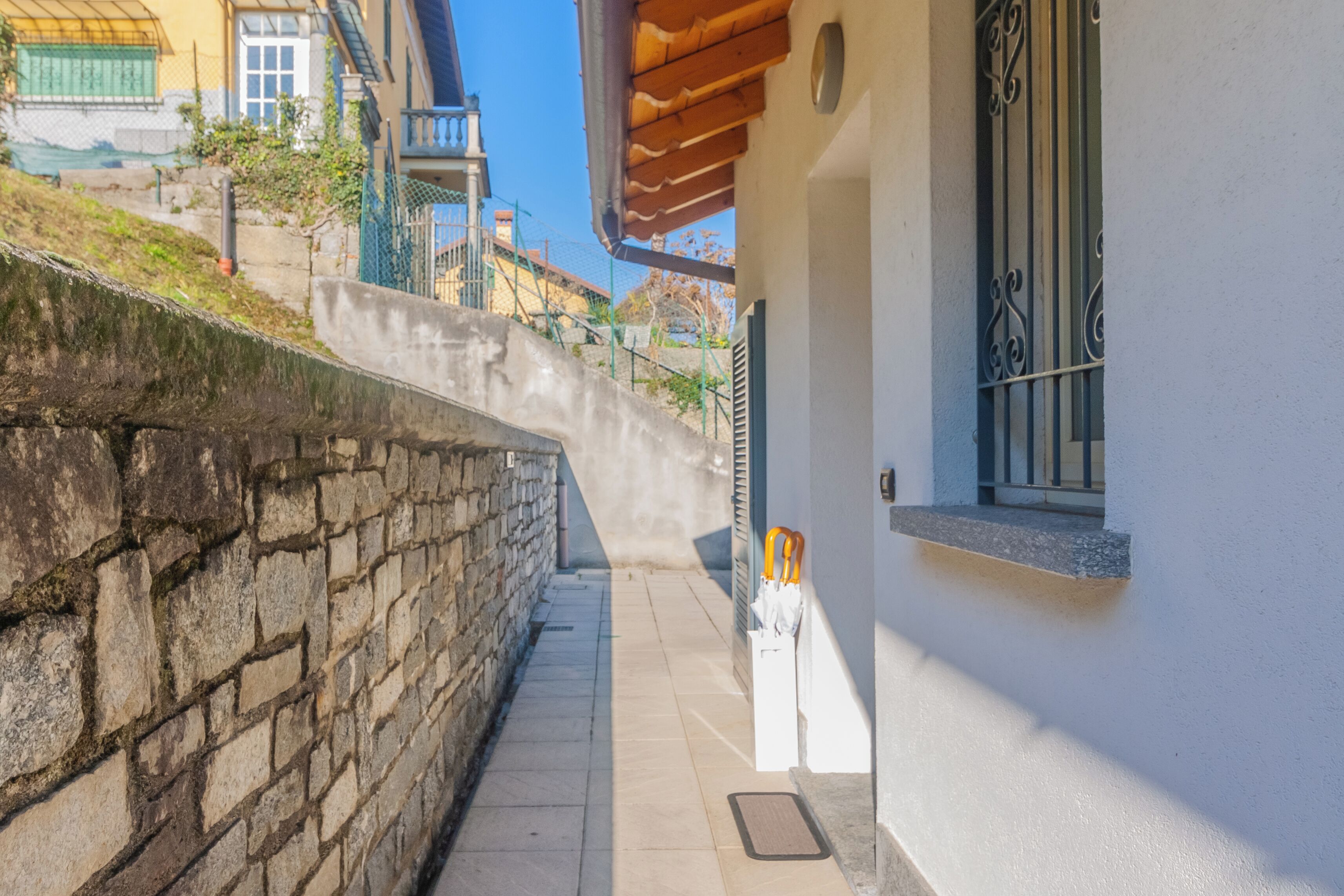 Un estrecho sendero de piedra que lleva a un edificio con fachada blanca y una ventana con rejas.
