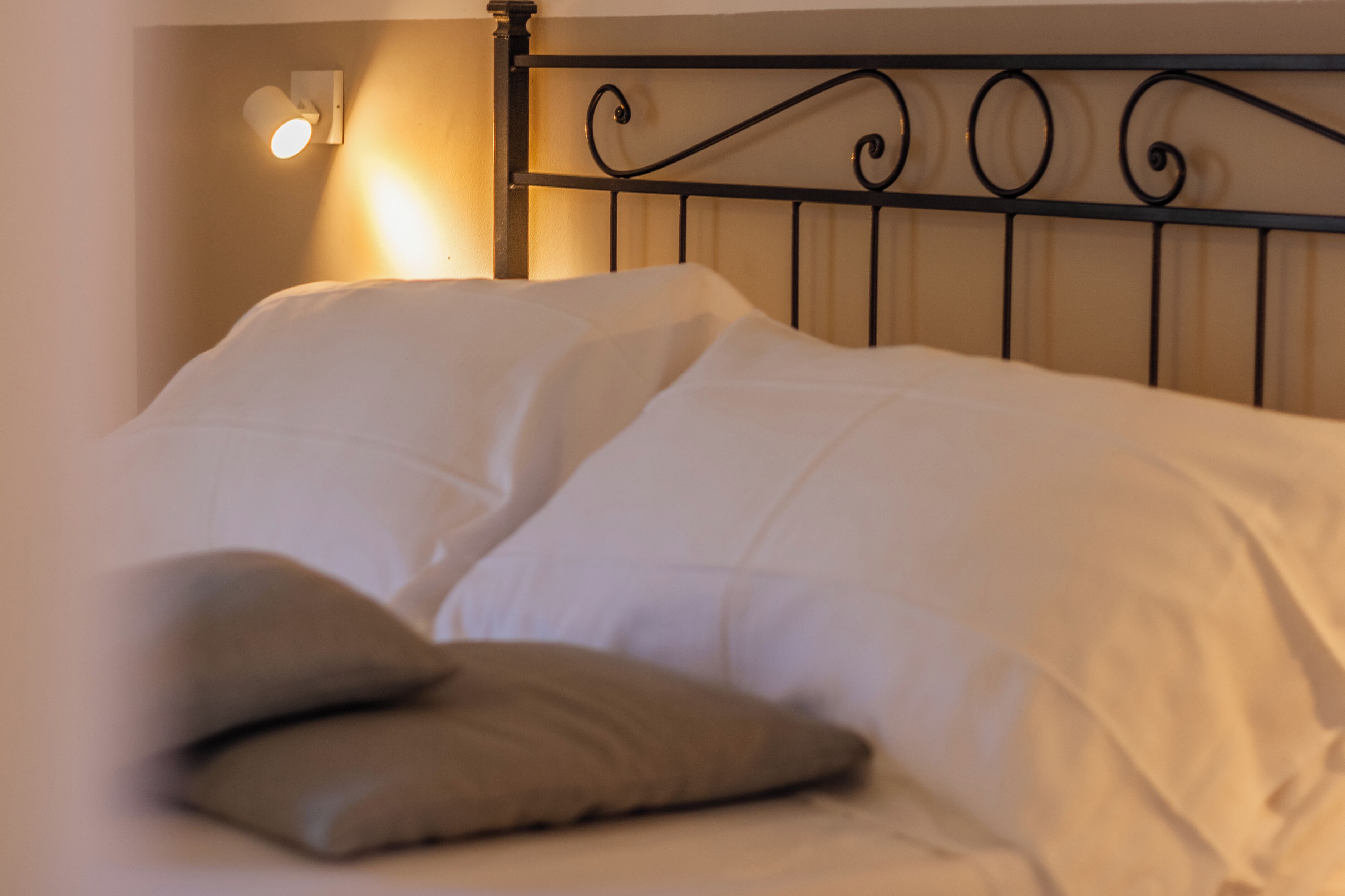 A neatly made bed with white linens and two pillows, a black metal headboard, and a wall-mounted light fixture.