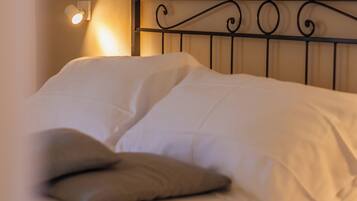A neatly made bed with white linens and two pillows, a black metal headboard, and a wall-mounted light fixture.