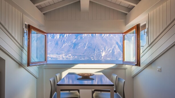 Ein Essbereich mit Tisch und Stühlen, ein Fenster mit Blick auf eine Stadtlandschaft und eine Holzbalkendecke.