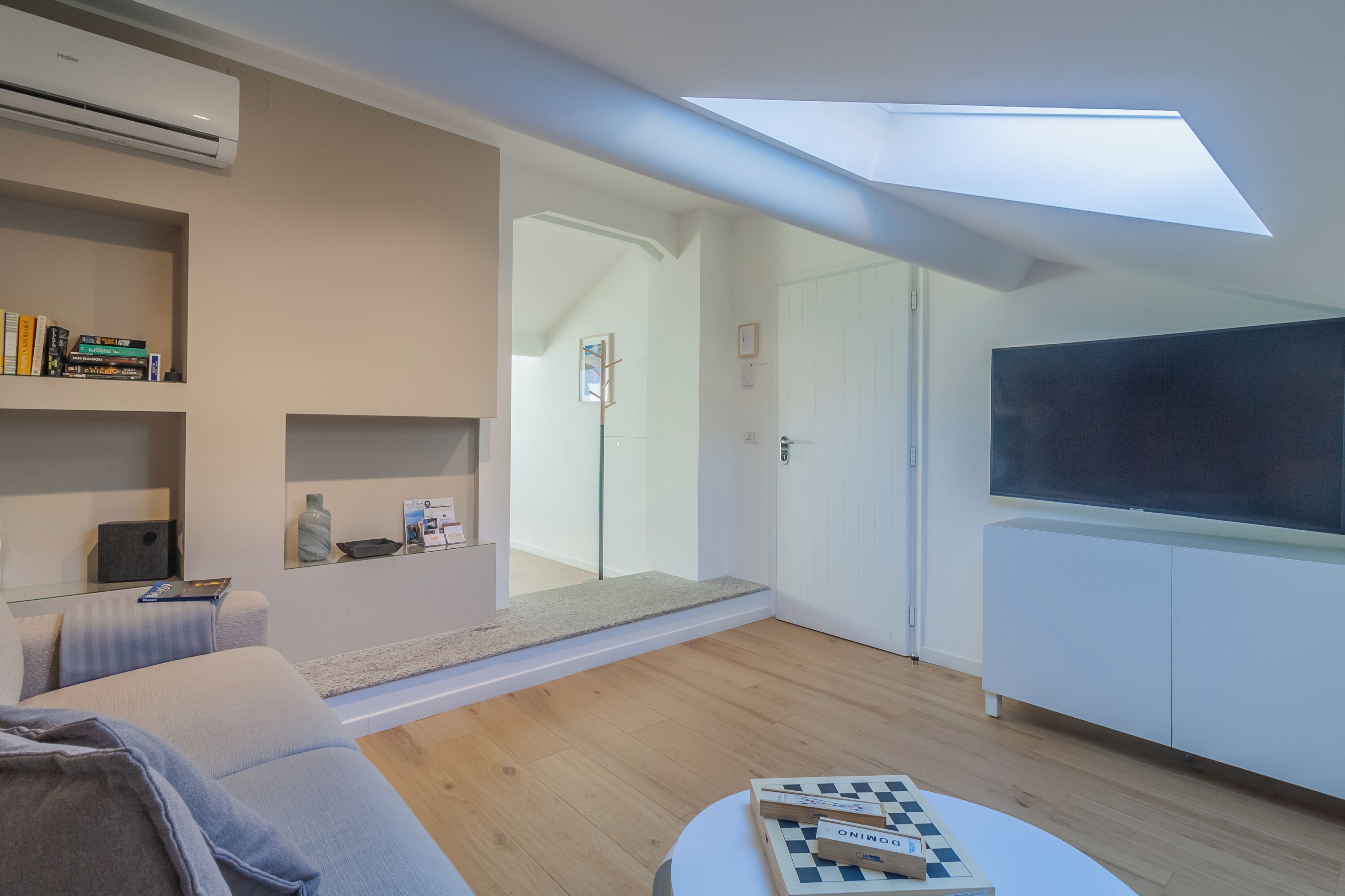 Una sala de estar moderna con tragaluz, un televisor de pantalla plana, un sofá y una mesa de centro con un juego de ajedrez.