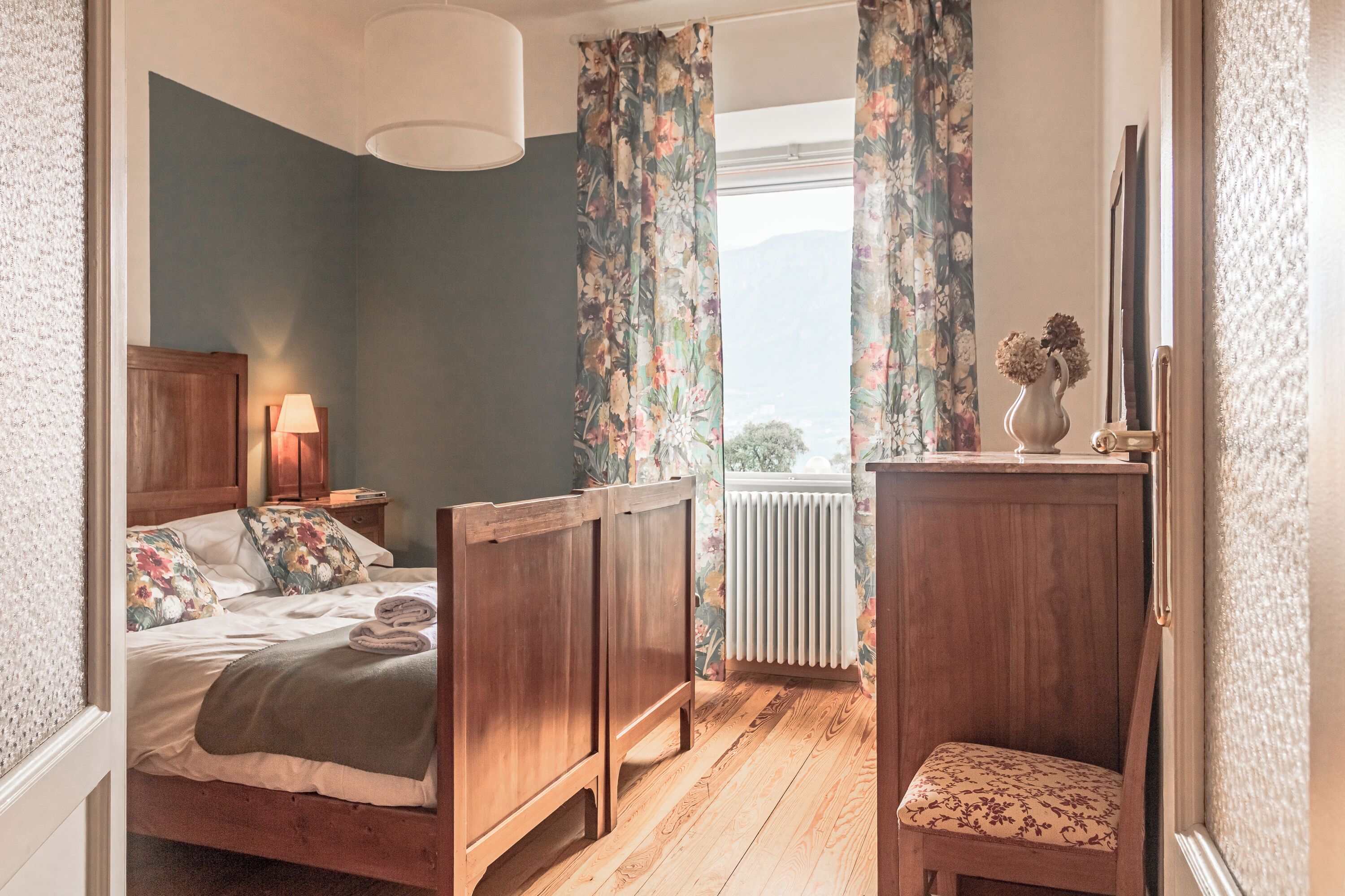 Ein Schlafzimmer mit einem Holzbett, einem Nachttisch, einer Kommode und einem Fenster mit Vorhängen.