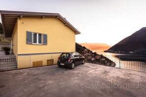 Un bâtiment jaune avec une voiture garée devant, une rambarde en métal et, au loin, une étendue d’eau et des collines.