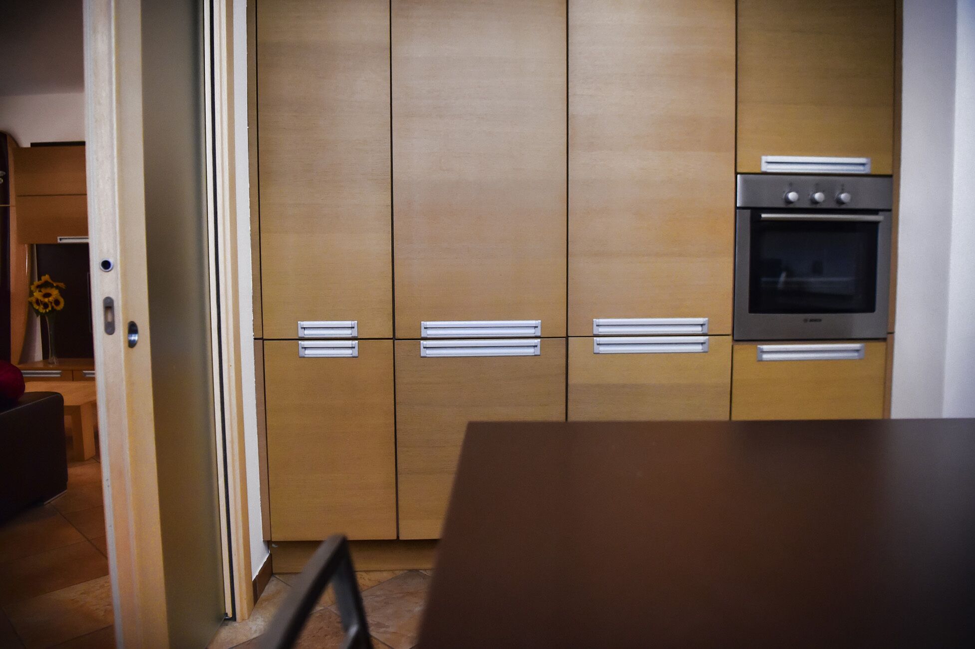 Een keuken met houten kastjes, een inbouwoven en een eettafel.