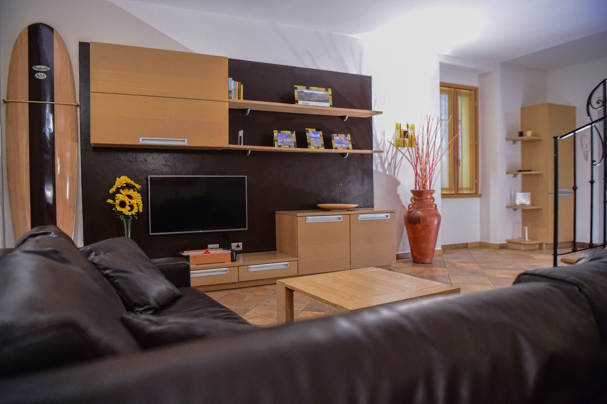 Een moderne woonkamer met een bank, televisie, houten kasten en een decoratieve vaas.