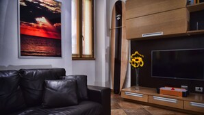 Un moderno salón con un sofá de cuero, un televisor de pantalla plana grande, un mueble de madera y un cuadro con una puesta de sol.