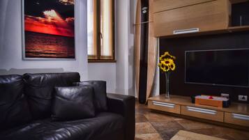 Een moderne woonkamer met een leren bank, een grote flatscreen-tv, een houten kast en een schilderij van een zonsondergang in een lijst.