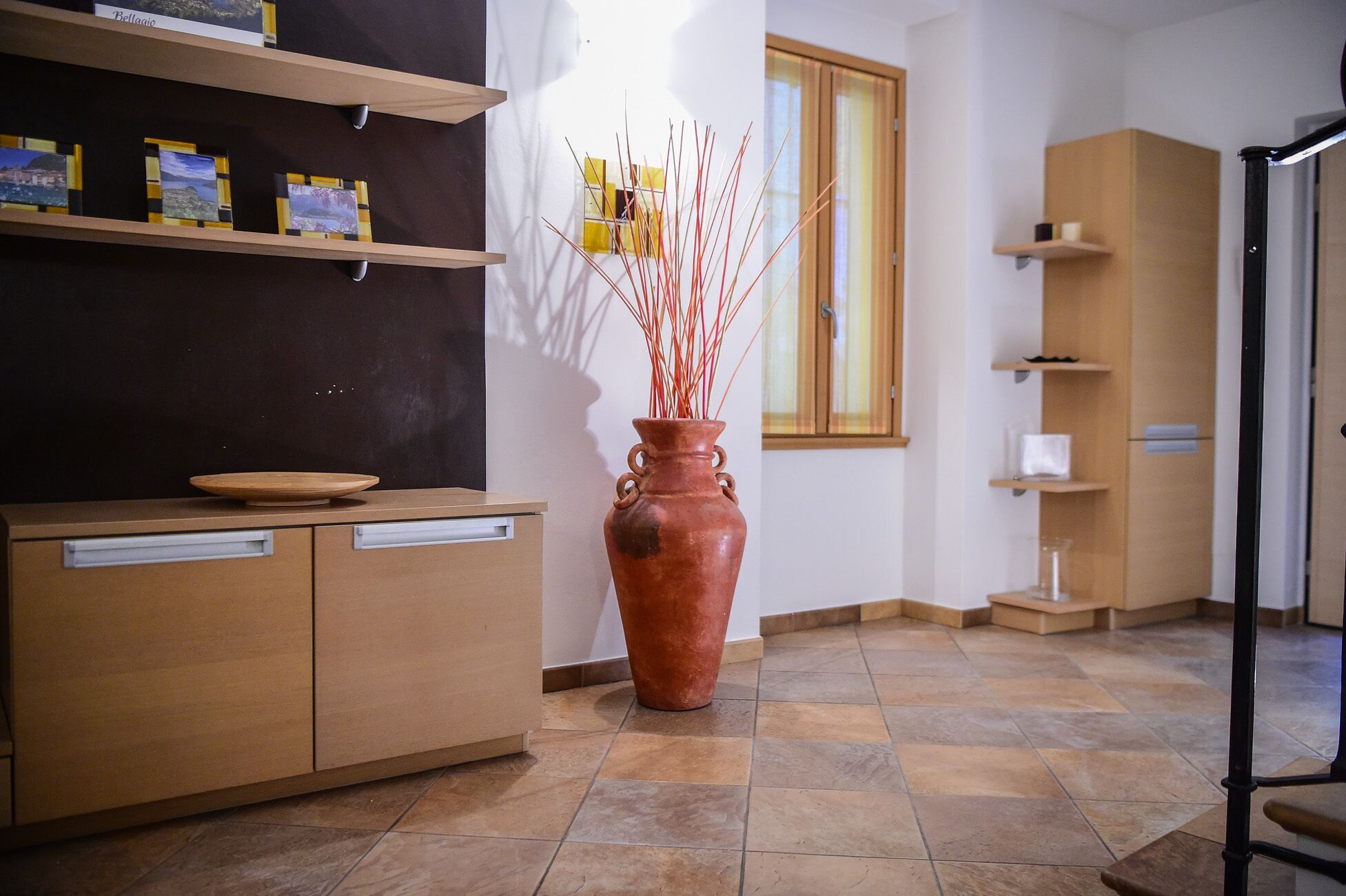 Eine Küche mit einem Holzkasten, einer großen Terrakotta-Vase mit Zweigen und einem Fenster mit Vorhängen.