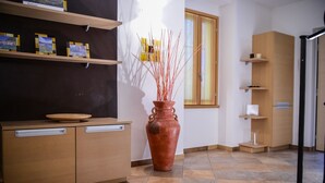 Una cocina con un armario de madera, un jarrón de terracota grande con ramas y una ventana con cortinas.