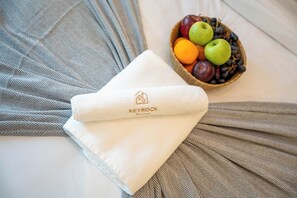 A neatly folded white towel with a logo on a bed with patterned bedding. - Elegant Reva 1BR - Pool & Gym (Dubai)
