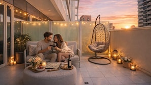 A couple on a balcony with a hanging chair, string lights, and candles. - Elegant Reva 1BR - Pool & Gym (Dubai)