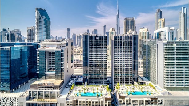 A high-rise hotel with a rooftop pool area, surrounded by modern skyscrapers. - Elegant Reva 1BR - Pool & Gym (Dubai)