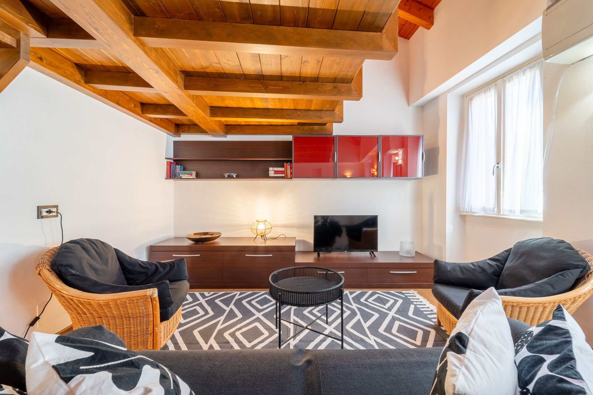 Ein modernes Wohnzimmer mit Holzboden, einem Fernseher und einer Sitzecke mit einem gemusterten Teppich.