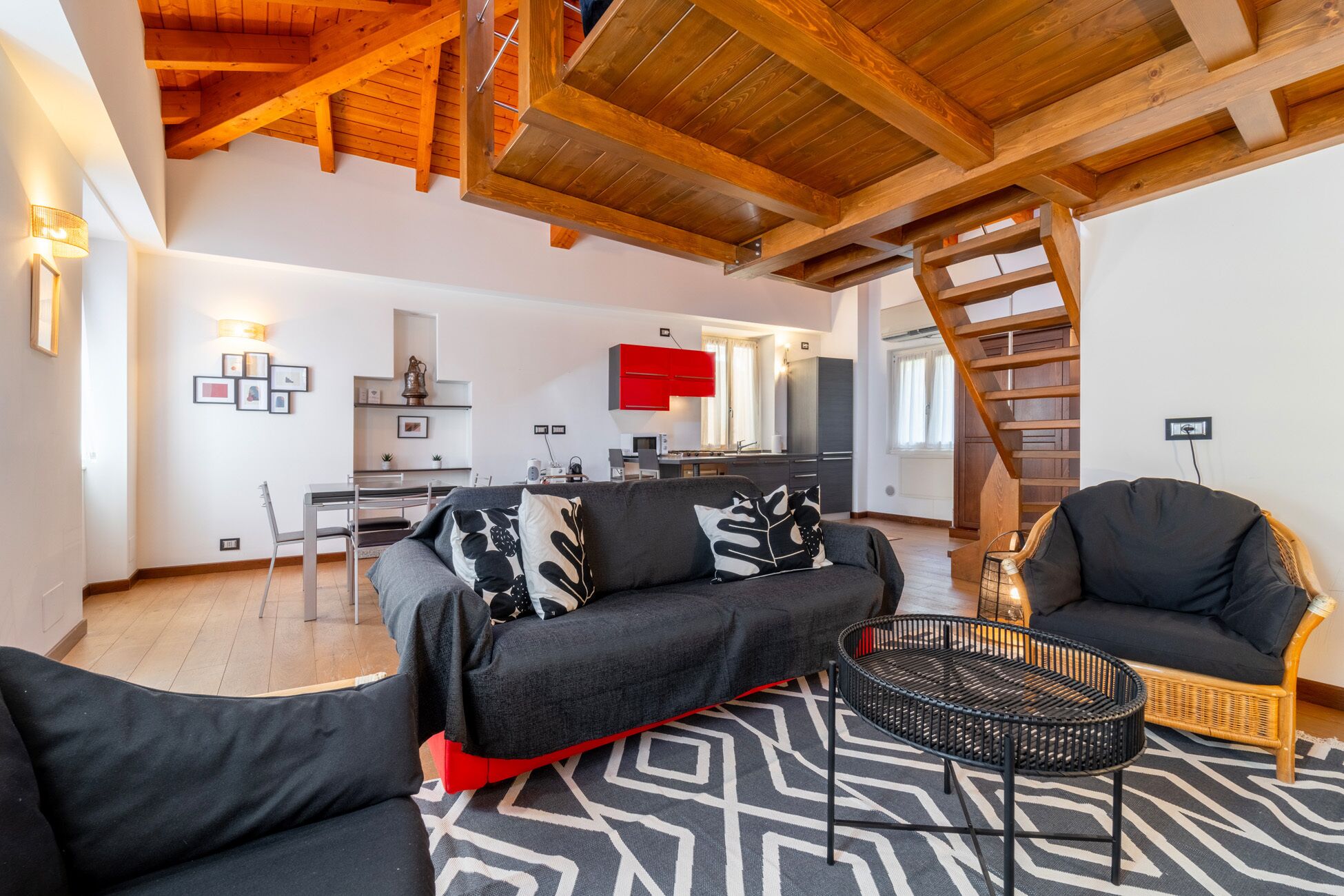 Ein modernes Wohnzimmer mit Sofa, Sessel, Couchtisch und einer Treppe, die in ein Obergeschoss führt.