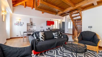 Ein modernes Wohnzimmer mit Sofa, Sessel, Couchtisch und einer Treppe, die in ein Obergeschoss führt.