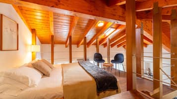 Ein Zimmer mit hohen Decken, einer Holzbalkendecke, einem Bett, zwei Stühlen und einem kleinen Tisch.