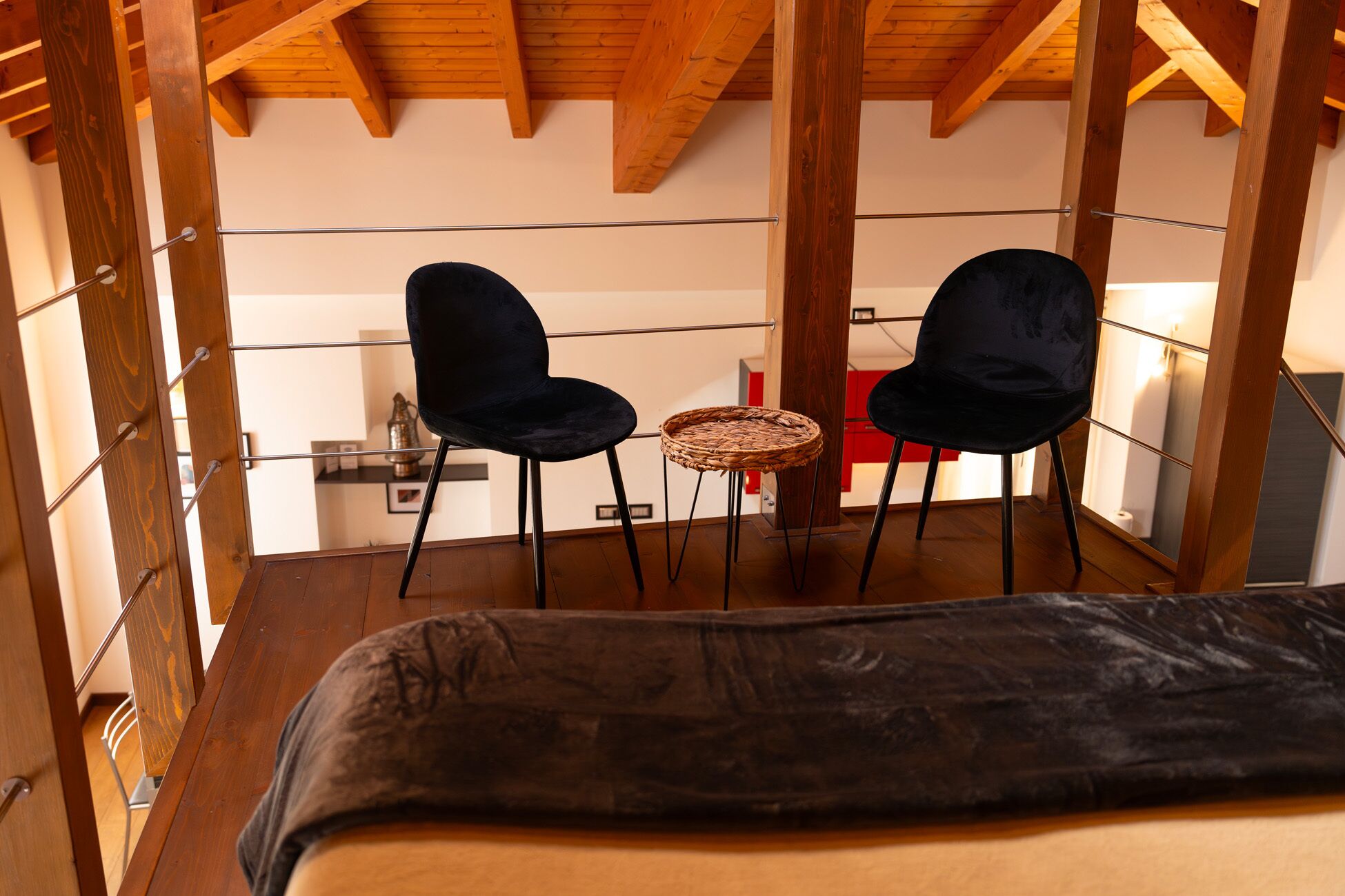 Ein Zimmer mit einem Bett, zwei schwarzen Stühlen und einem kleinen runden Tisch mit Flechtwerkplatte.