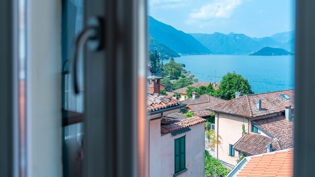 Une vue sur un lac, avec des montagnes en arrière-plan, une ville aux toits de tuiles et un aperçu d’un bâtiment doté d’une fenêtre.
