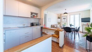 Une cuisine moderne avec des meubles blancs, un plan de travail en bois et un coin repas comprenant une table et des chaises.