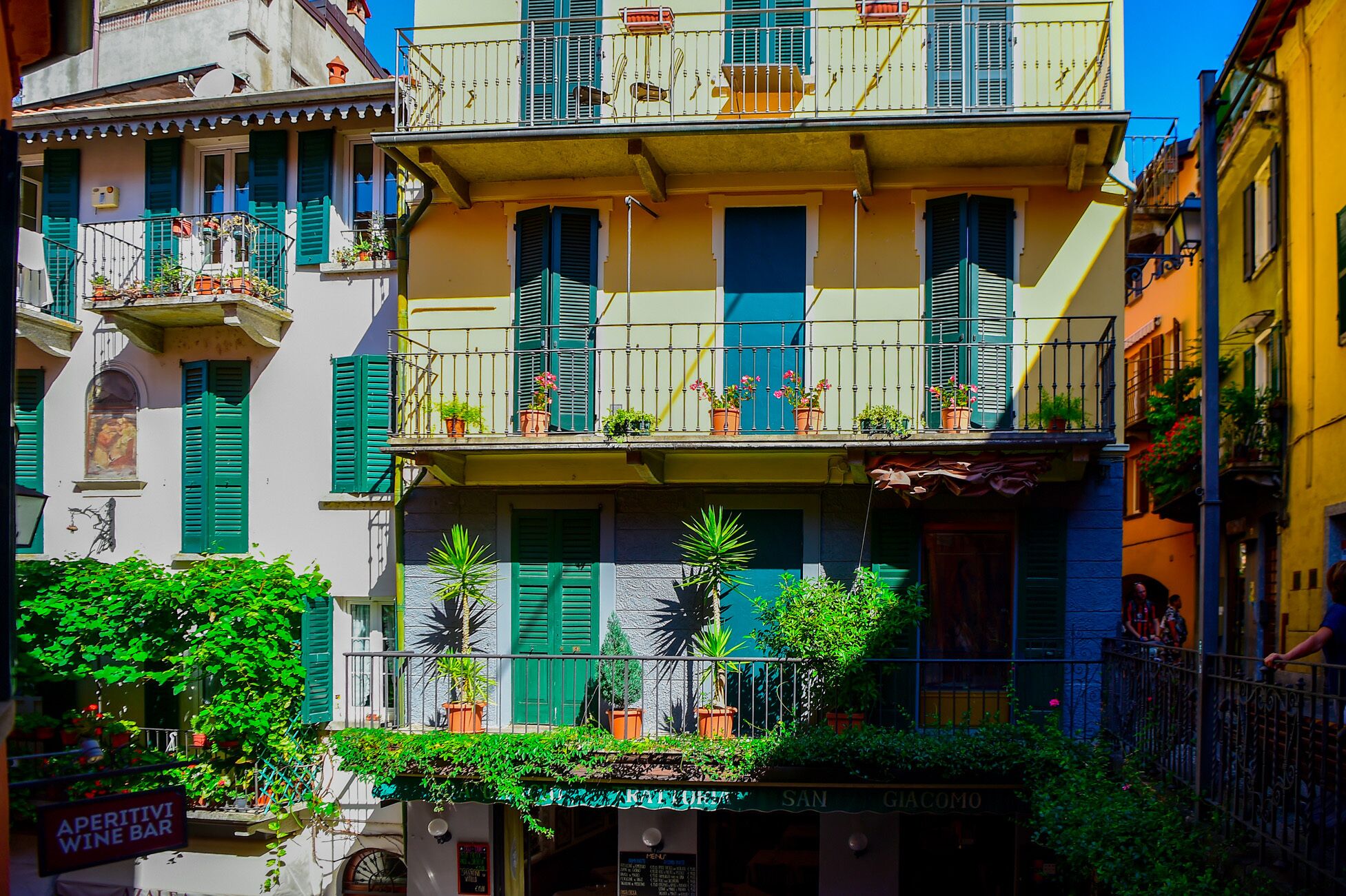 Un edificio de varios pisos con balcones, plantas en macetas y un cartel que dice 'Aperitivi Wine Bar'.