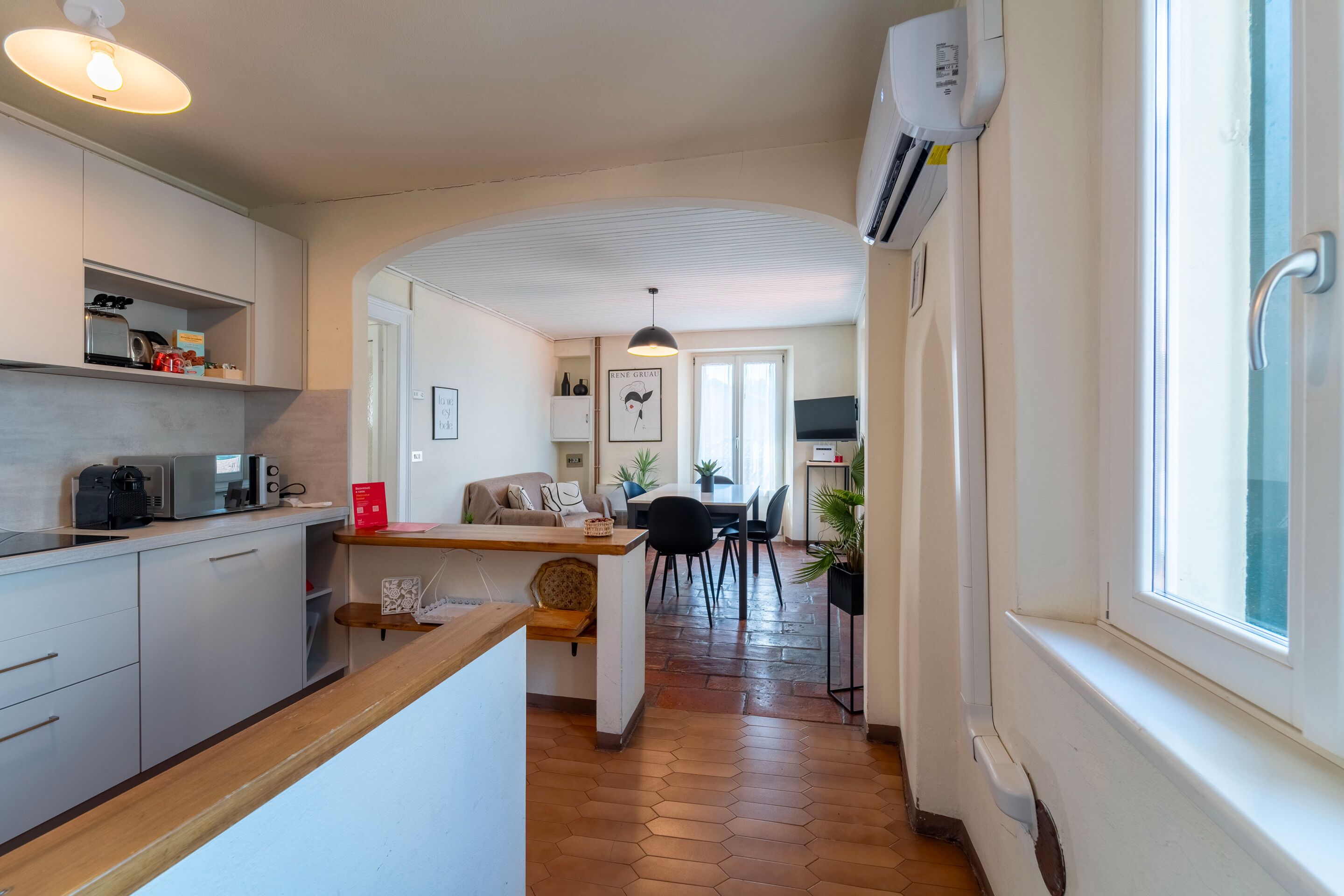 A modern kitchen with a wooden countertop, a dining area with a table and chairs, and a hallway leading to a living room.