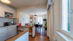 Une cuisine moderne avec un plan de travail en bois, un coin repas comprenant une table et des chaises, et un couloir menant au salon.