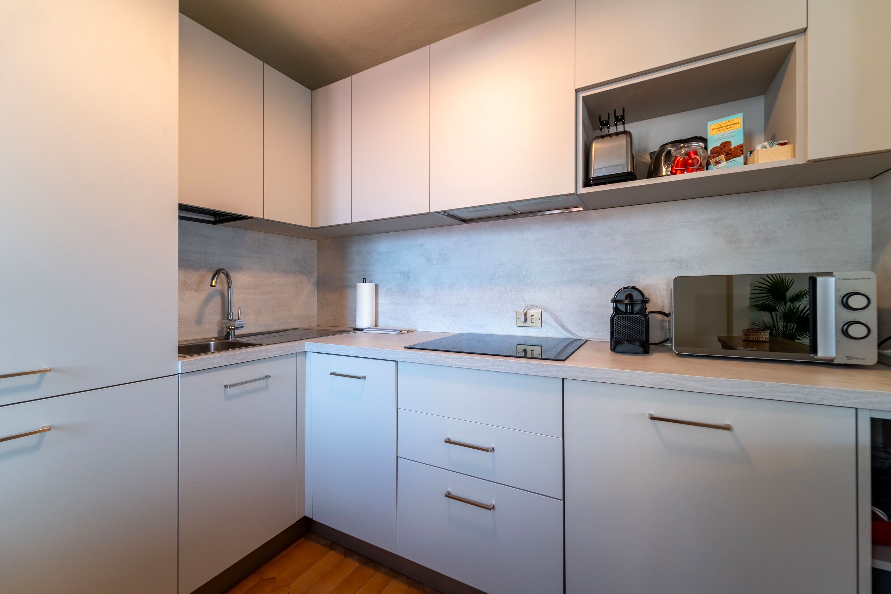 Een moderne keuken met witte kasten, een roestvrijstalen spoelbak, een magnetron en een plank met keukengerei.