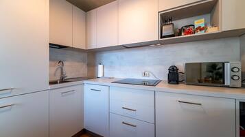 Een moderne keuken met witte kasten, een roestvrijstalen spoelbak, een magnetron en een plank met keukengerei.
