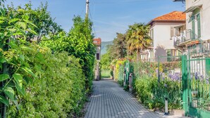 A narrow paved pathway flanked by lush greenery and residential buildings with visible balconies and windows.