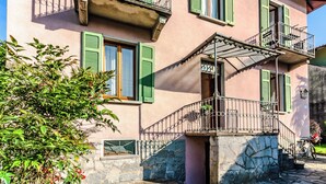 A pink building with green shutters, a stone staircase, and a metal railing.