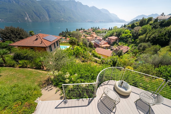 Zona residencial con vista a un lago y montañas, con una casa que tiene piscina y terraza con mobiliario exterior.
