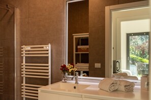 A bathroom with a white sink, a mirror, a towel rack, and a vase with flowers. - Zinnia Lakeview Apartment (Bellagio)