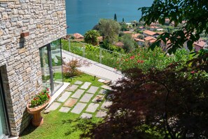 A modern building with a stone facade, a glass door, and a small garden with a pathway. - Zinnia Lakeview Apartment (Bellagio)