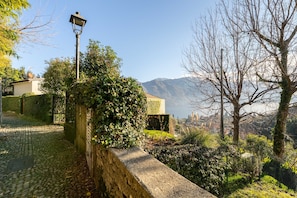A cobblestone pathway leading to a building with a lamp post and a view of mountains in the background. - Zinnia Lakeview Apartment (Bellagio)