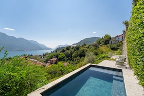 Piscina con agua cristalina, rodeada de exuberante vegetación y con vistas a un paisaje montañoso con un lago.