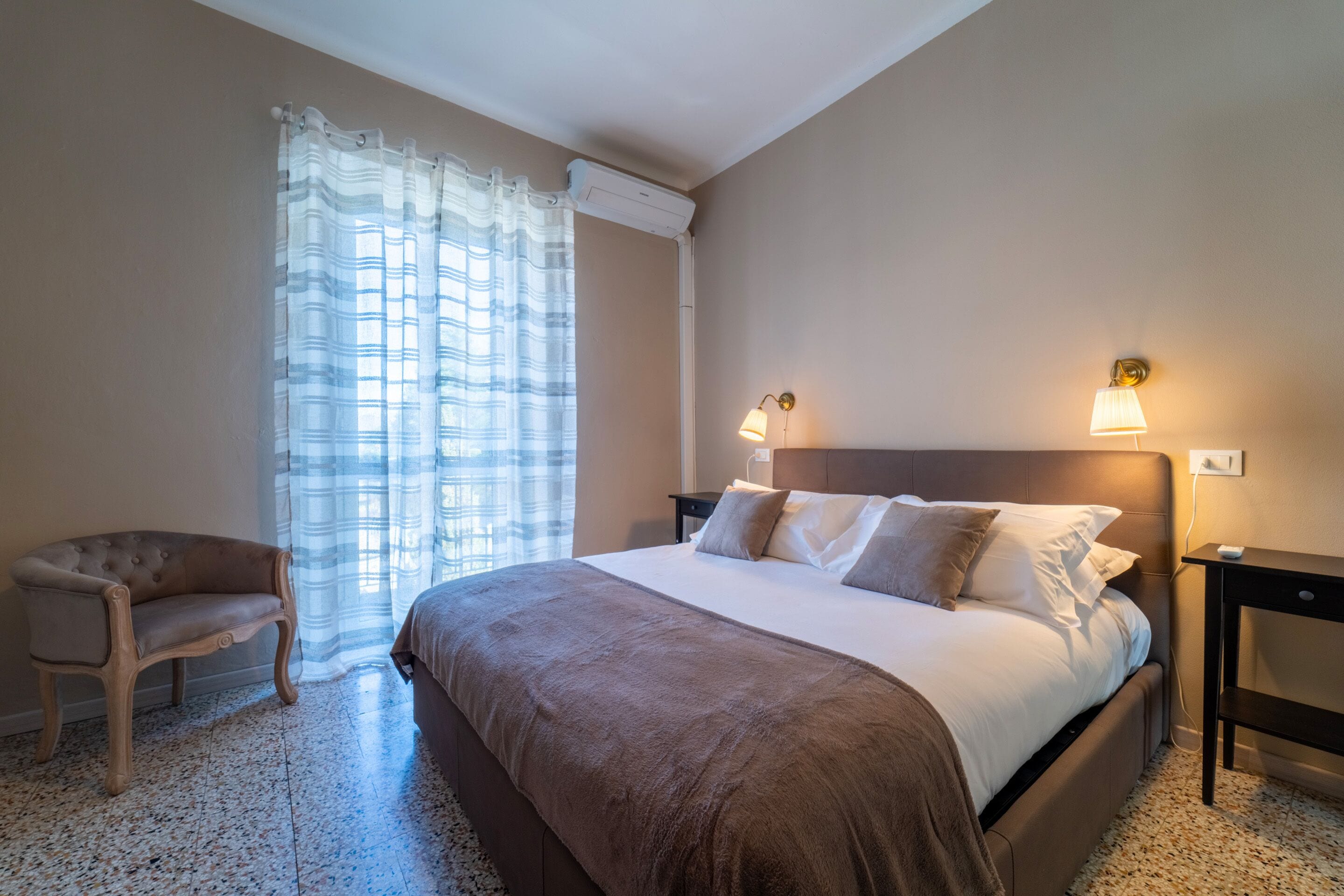 A bedroom with a bed, two bedside lamps, a chair, and a window with curtains.
