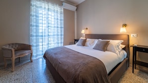 Une chambre à coucher avec un lit, deux lampes de chevet, une chaise et une fenêtre avec des rideaux.