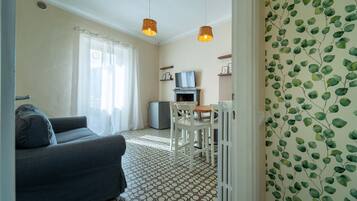 A living room with a sofa, a dining table with chairs, a television, and a small refrigerator.