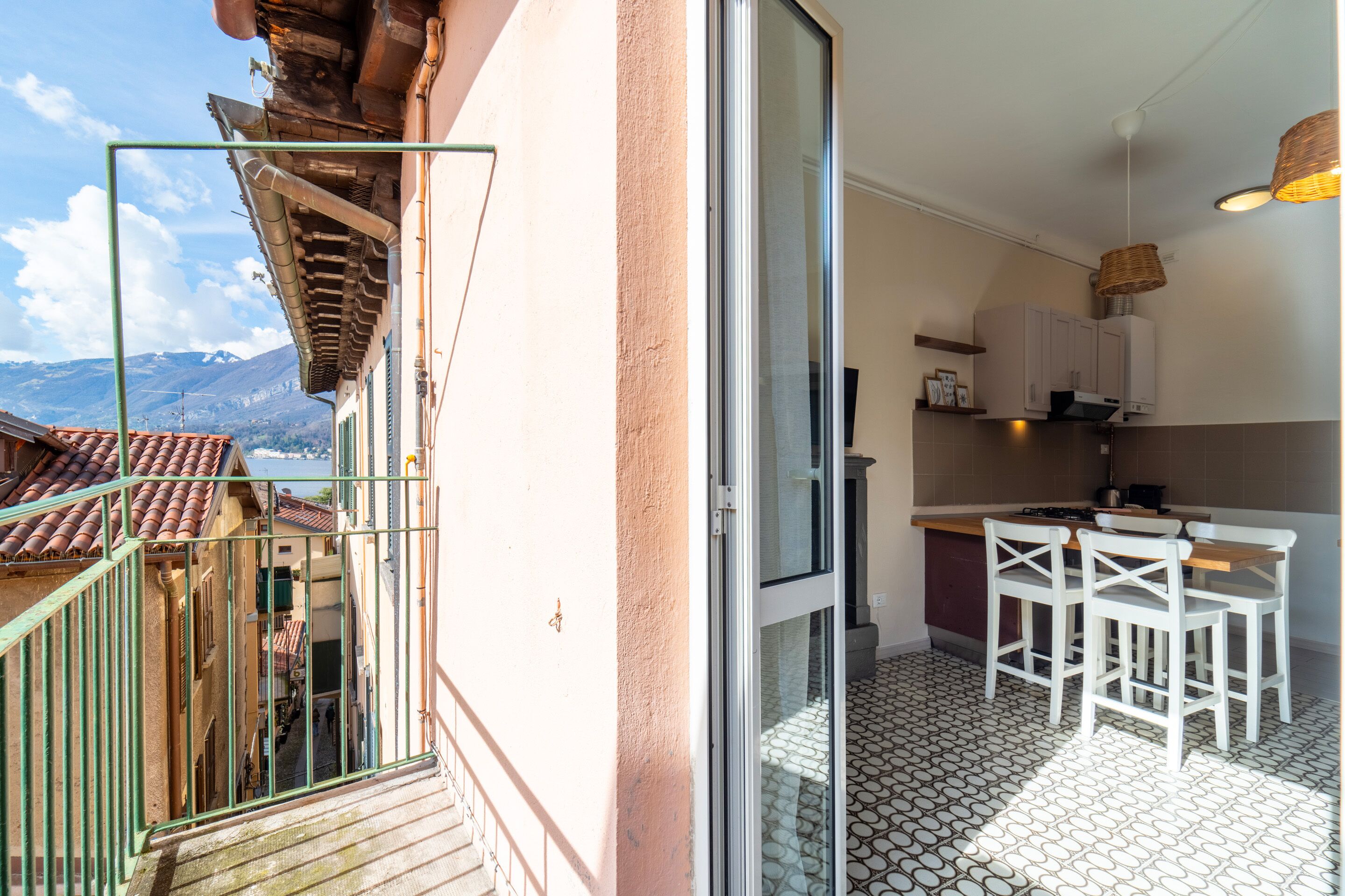 A balcony with a view of mountains, a kitchen with white cabinets and a dining area with white chairs.