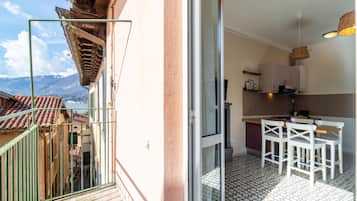 A balcony with a view of mountains, a kitchen with white cabinets and a dining area with white chairs.