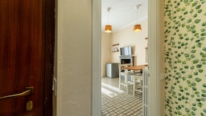 Un couloir avec une porte en bois, un radiateur, une petite table avec une chaise et un téléviseur posé sur un meuble.